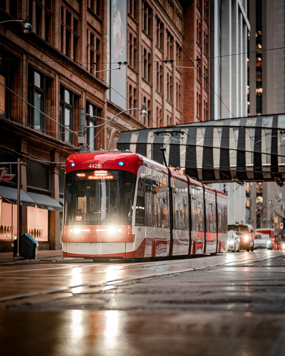 a red and white train traveling down a street next to tall buildings