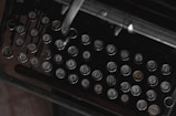 A close-up view of an antique typewriter with Cyrillic alphabet keys. The keys are round and metallic, featuring raised letters and numbers. The setting appears dark and vintage, highlighting the aged and historical aspect of the machine.
