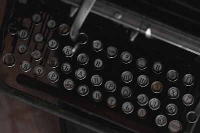 A close-up view of an antique typewriter with Cyrillic alphabet keys. The keys are round and metallic, featuring raised letters and numbers. The setting appears dark and vintage, highlighting the aged and historical aspect of the machine.