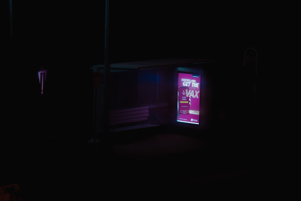 a bus stop in the dark with a neon sign