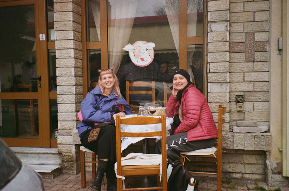 two women sitting at a table outside of a restaurant