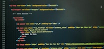 A computer screen displaying code with HTML-like tags and inline CSS styles. The code featured includes elements such as mj-body, mj-wrapper, and mj-text with specific styling for background colors, padding, alignment, and text content. Notable text within the code includes 'The Wait Is Over.'