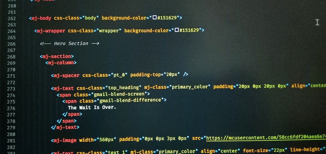 A computer screen displaying code with HTML-like tags and inline CSS styles. The code featured includes elements such as mj-body, mj-wrapper, and mj-text with specific styling for background colors, padding, alignment, and text content. Notable text within the code includes 'The Wait Is Over.'
