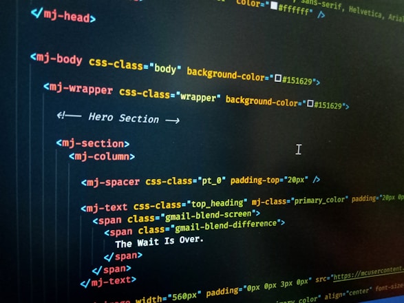 HTML code displayed on a computer screen, featuring elements such as 'mj-body', 'mj-wrapper', and 'mj-text'. The code includes CSS classes for styling purposes, indicating colors with hex codes like '#151629'. A comment suggests this section is the 'Hero Section'.