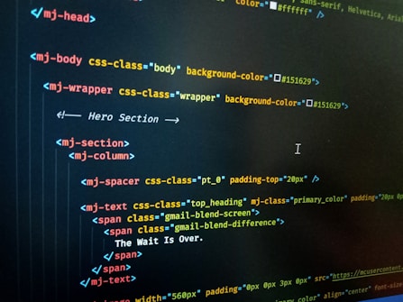 HTML code displayed on a computer screen, featuring elements such as 'mj-body', 'mj-wrapper', and 'mj-text'. The code includes CSS classes for styling purposes, indicating colors with hex codes like '#151629'. A comment suggests this section is the 'Hero Section'.