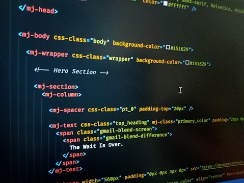 HTML code displayed on a computer screen, featuring elements such as 'mj-body', 'mj-wrapper', and 'mj-text'. The code includes CSS classes for styling purposes, indicating colors with hex codes like '#151629'. A comment suggests this section is the 'Hero Section'.