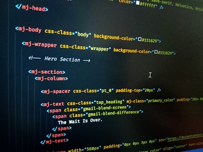 HTML code displayed on a computer screen, featuring elements such as 'mj-body', 'mj-wrapper', and 'mj-text'. The code includes CSS classes for styling purposes, indicating colors with hex codes like '#151629'. A comment suggests this section is the 'Hero Section'.