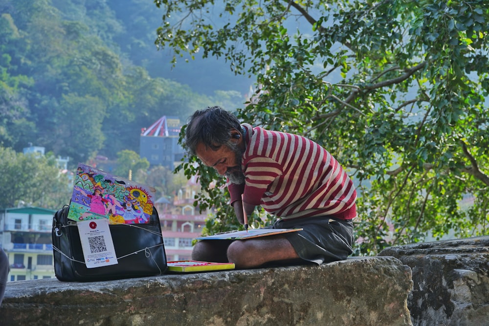 a man sitting on a ledge reading a book