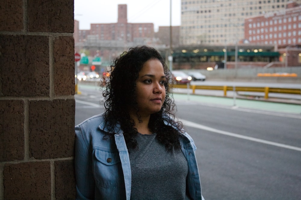 a woman standing next to a brick wall