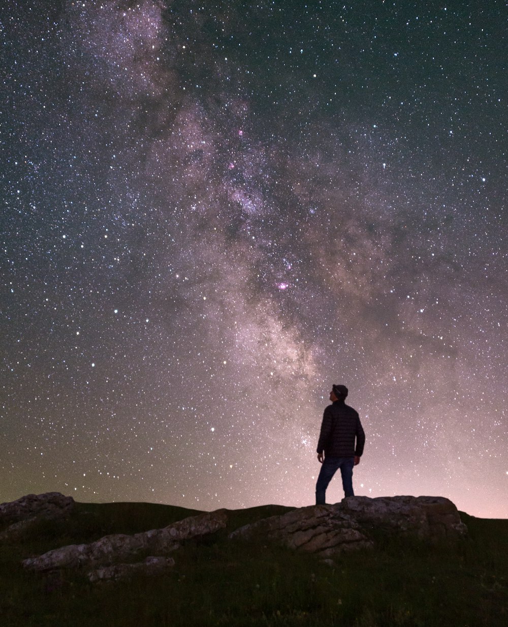 a man standing on top of a hill under a night sky filled with stars