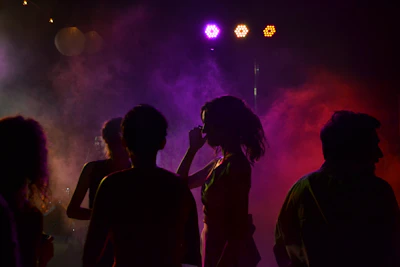 Wide shot of a nighttime party scene with vibrant lighting and energetic crowd.