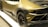 A luxury sports car with a sleek design, featuring a matte gold finish and black accents. The car has a distinctive rear section with aerodynamic elements and large black alloy wheels. The tire treads are distinctly visible, and a V10 badge is spotted near the engine cover.