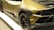 A luxury sports car with a sleek design, featuring a matte gold finish and black accents. The car has a distinctive rear section with aerodynamic elements and large black alloy wheels. The tire treads are distinctly visible, and a V10 badge is spotted near the engine cover.