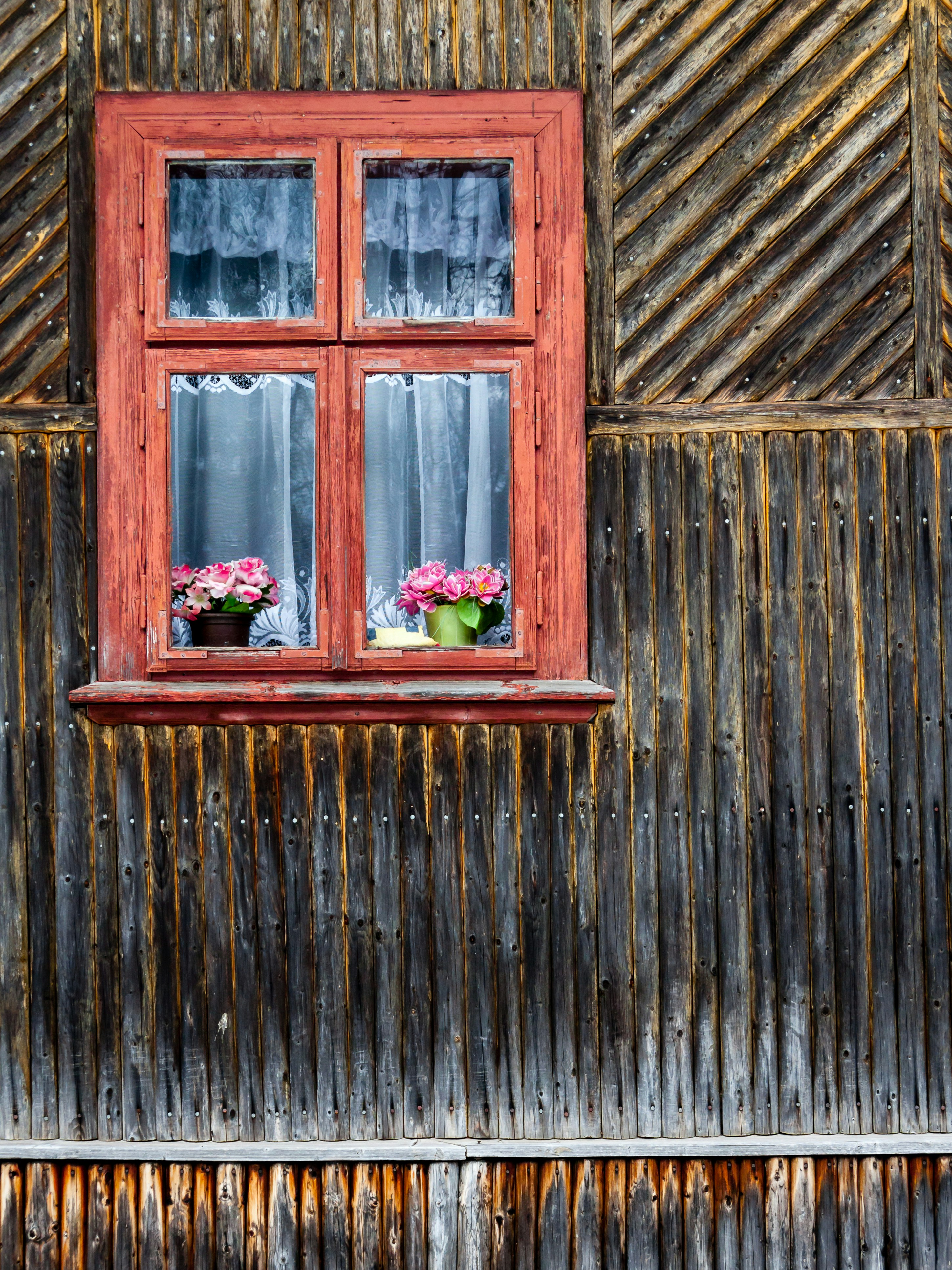 a wooden wall with a red window and flowers in the window