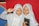 Two young girls wearing white hijabs are smiling. The girl on the left is holding a book with 'jeda' on the cover, while the girl on the right is holding a book with '00.00' on the cover. They are standing in front of a colorful backdrop featuring red, blue, and yellow sections.