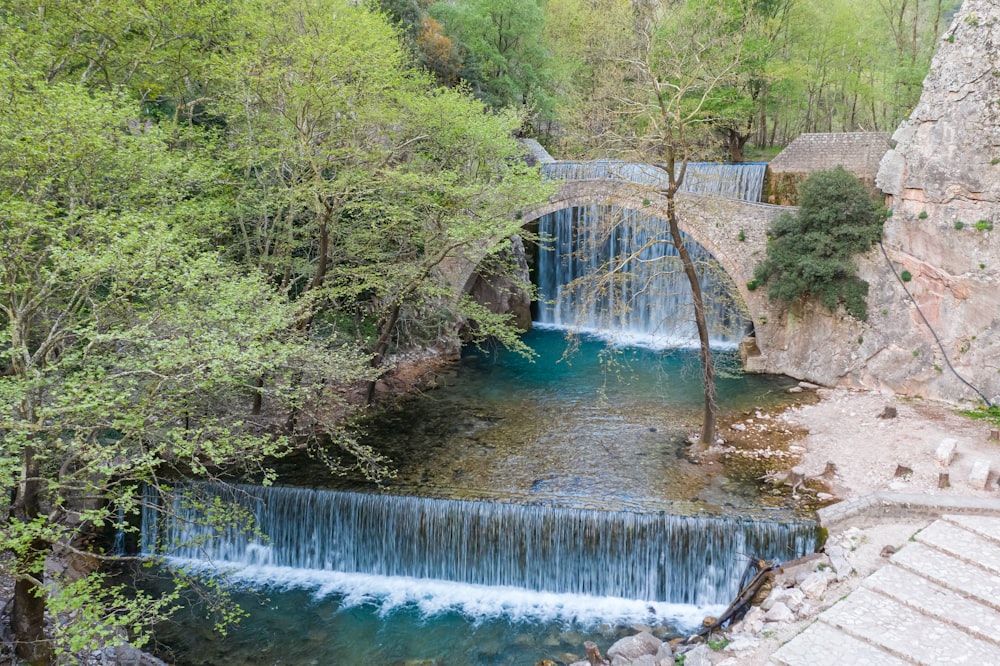 a waterfall flowing under a bridge next to a forest