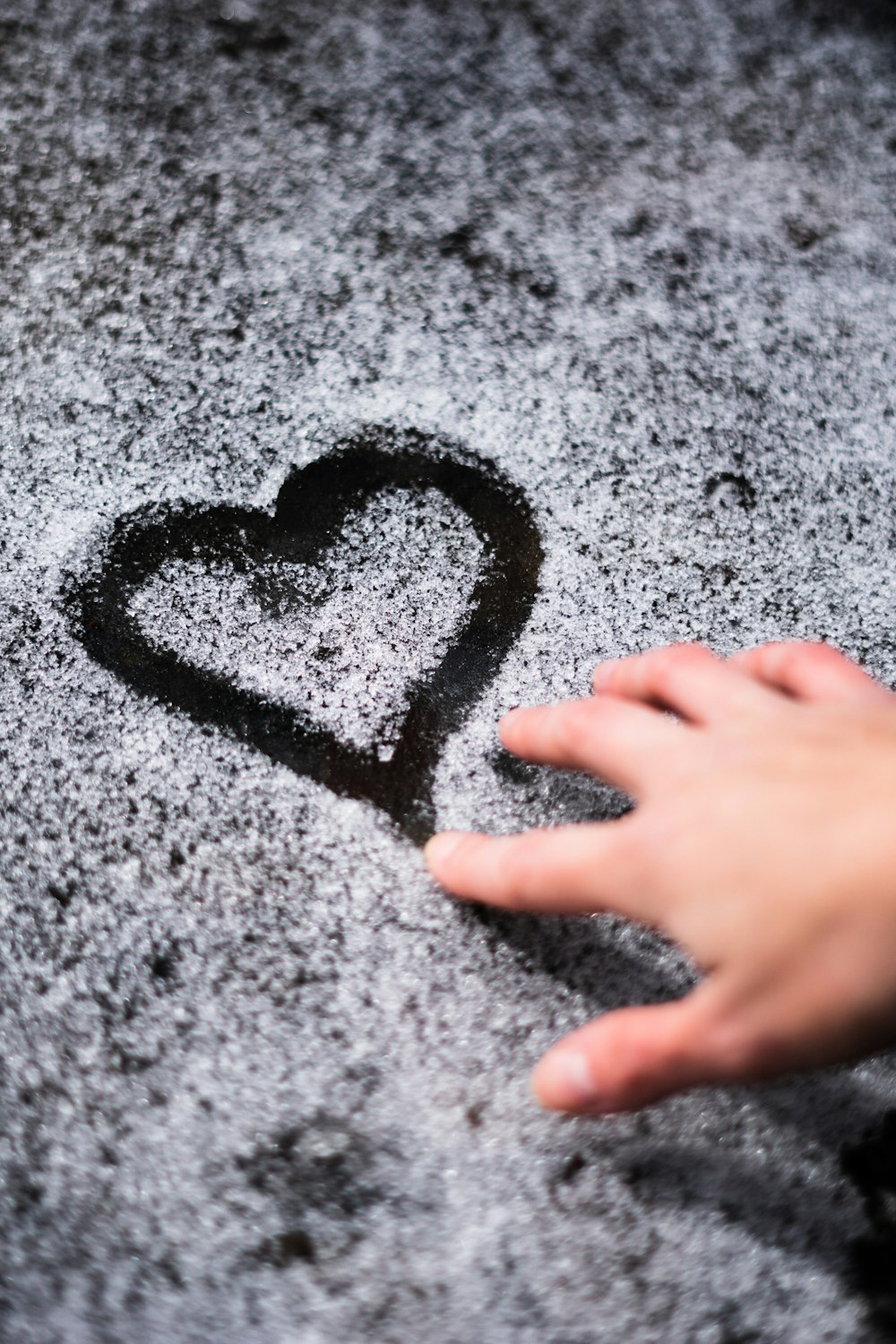 a person's hand touching a heart drawn in the snow