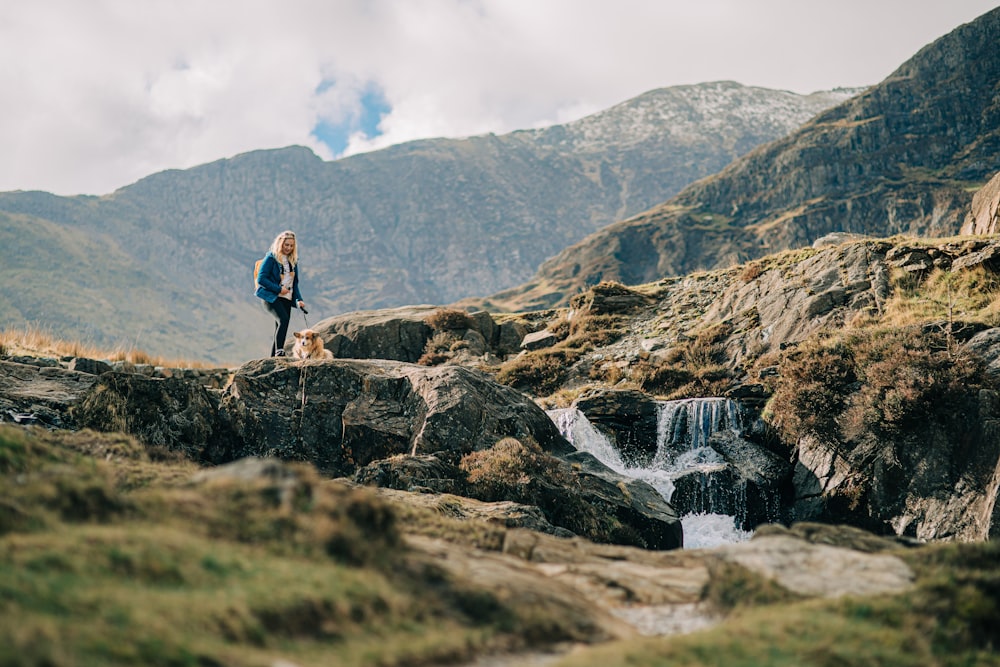 a woman standing on top of a mountain next to a waterfall