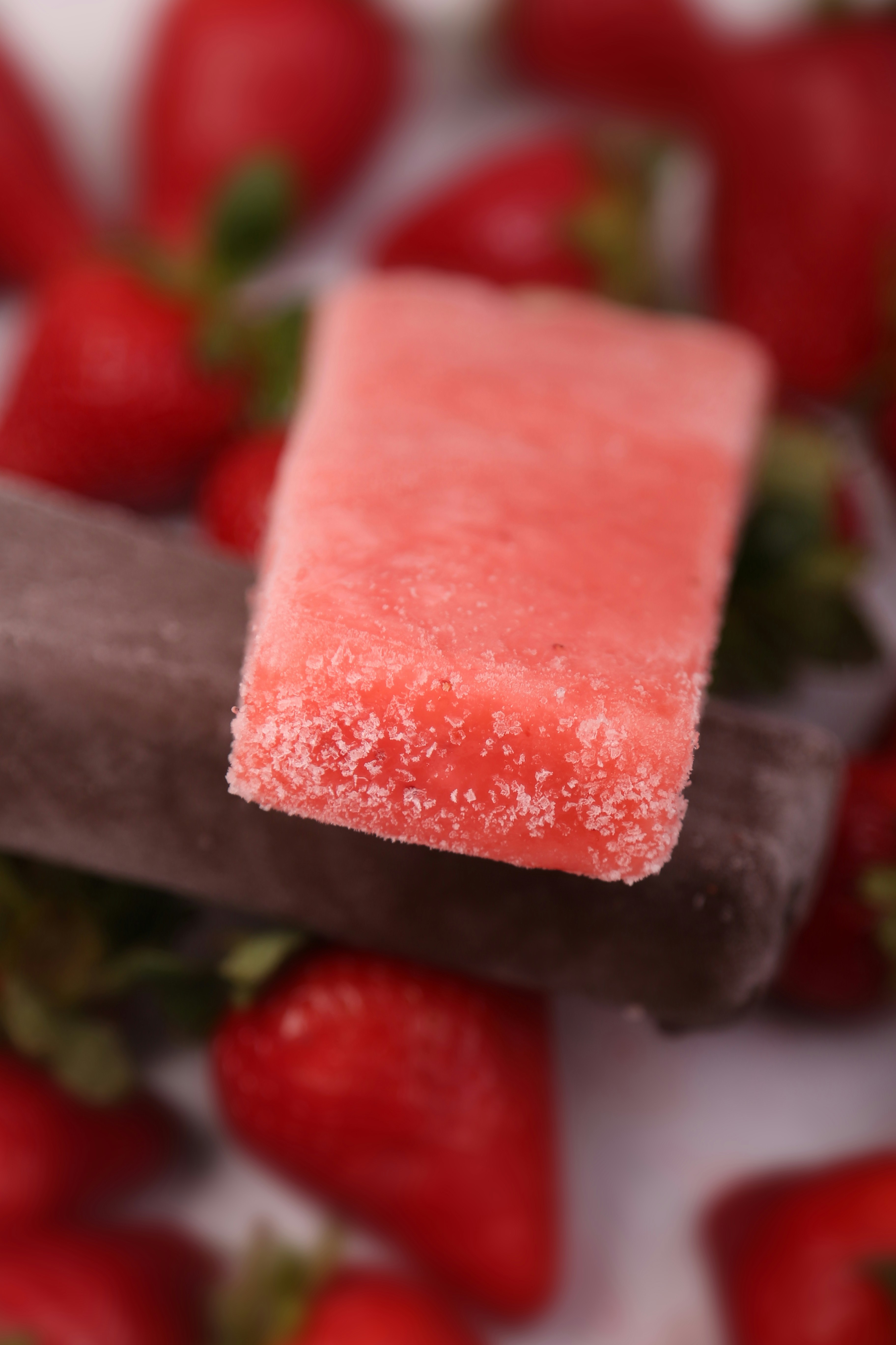 a close up of a sugary popsicle with strawberries in the background