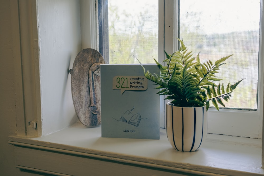 a book sitting on a window sill next to a potted plant