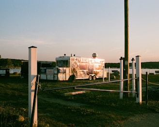 A sleek, modern food trailer parked at a bustling city food market during golden hour.
