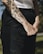 A close-up of a person's forearm with detailed black ink tattoos, featuring floral designs, scissors, and other objects. The person is wearing a white sleeveless top and dark pants.