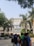 A group of students standing and chatting in front of a large academic building with a prominent entrance. The building is surrounded by palm trees, and the architecture is modern, featuring a large central display with the name 'Svit'. The sunny day casts clear shadows, and the atmosphere seems lively and bustling.