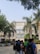 A group of students standing and chatting in front of a large academic building with a prominent entrance. The building is surrounded by palm trees, and the architecture is modern, featuring a large central display with the name 'Svit'. The sunny day casts clear shadows, and the atmosphere seems lively and bustling.