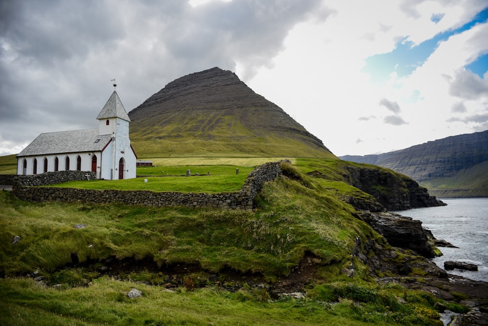 a small church on a grassy hill next to a body of water