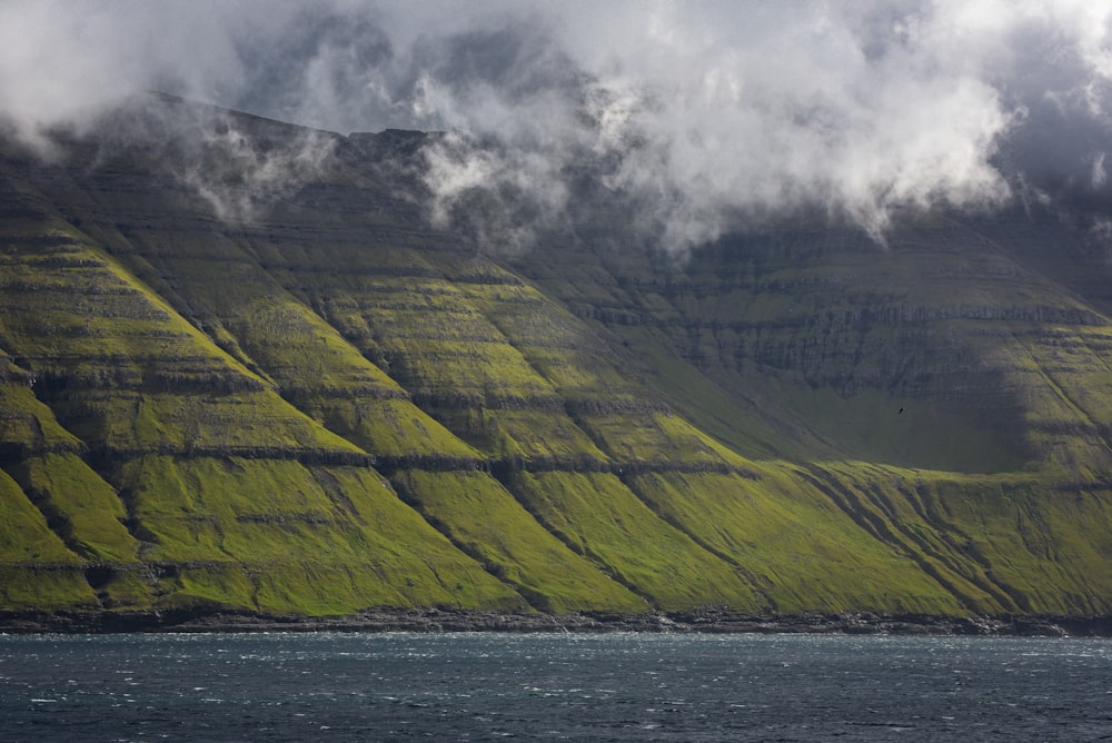 a green mountain with a body of water in front of it