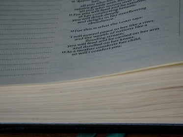 A close-up image of an open book displaying a passage with a religious or philosophical text. The text is printed in a clear, formal font on cream-colored pages, and the book appears thick and well-used.