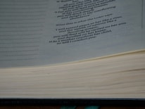 A close-up image of an open book displaying a passage with a religious or philosophical text. The text is printed in a clear, formal font on cream-colored pages, and the book appears thick and well-used.