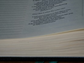A close-up image of an open book displaying a passage with a religious or philosophical text. The text is printed in a clear, formal font on cream-colored pages, and the book appears thick and well-used.