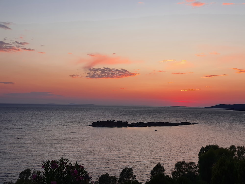 a sunset over a body of water with a small island in the middle