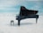 A grand piano stands prominently on a vast, open surface that resembles ice or a reflective floor. The background is a clear, expansive blue sky with a few light clouds, conveying a sense of calm and tranquility. The piano is black and polished, with a matching piano bench placed closely beside it.