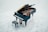 A grand piano with its lid open, showcasing the strings and internal components, placed on a light grey marble floor. There is a matching piano bench positioned in front of the piano.