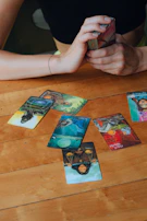 Close-up of hands shuffling tarot cards over a wooden table with astrological symbols.
