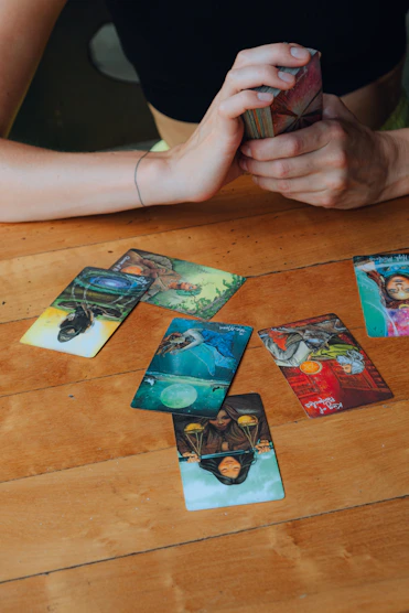 A close-up of hands gently shuffling tarot cards over a smooth wooden table.