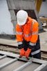 a man in an orange safety jacket working on a metal rail