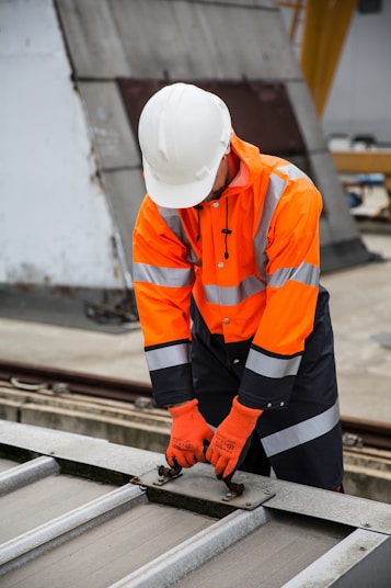 a man in an orange safety jacket working on a metal rail