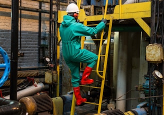 a man in a green coverall climbing up a yellow ladder