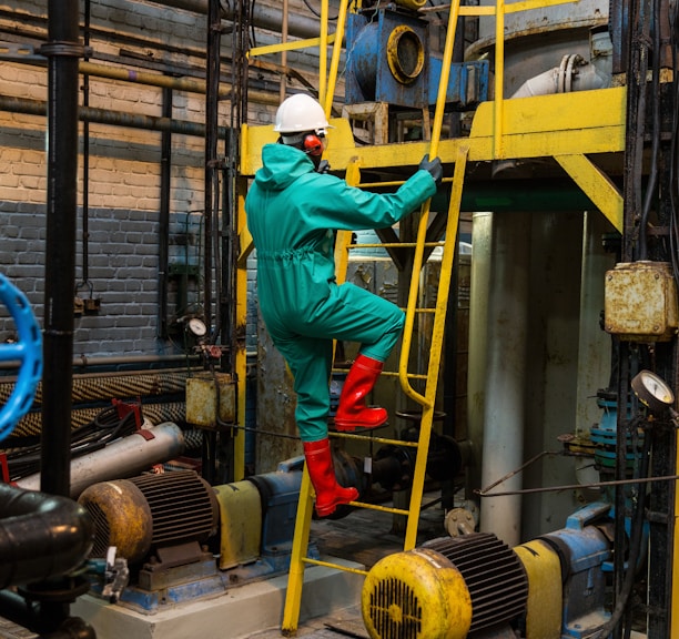 a man in a green coverall climbing up a yellow ladder