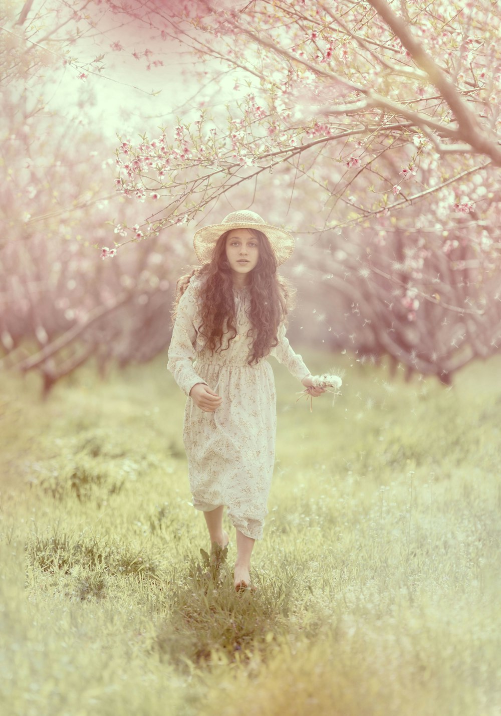 a woman in a white dress and hat walking through a field