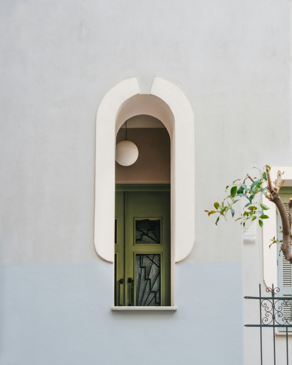 uma porta verde e um edifício branco com uma árvore na janela