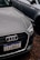 A close-up of the front of an Audi car with a Brazilian license plate, parked on a gravel surface. The Audi emblem is prominently visible on the front grille. The car is positioned next to another vehicle, which is partially visible in the background.