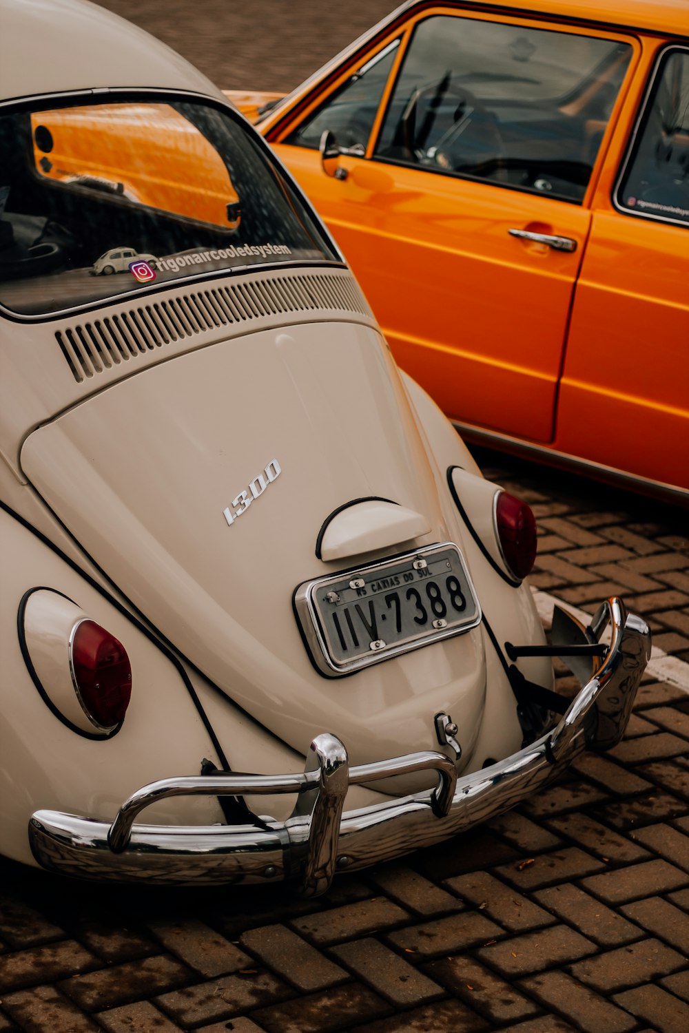 Un bug VW blanc garé à côté d’une voiture orange