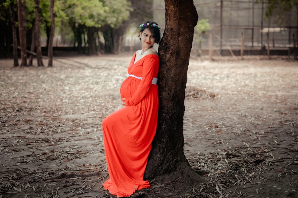 a woman in an orange dress leaning against a tree