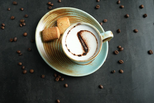 Steaming cup of coffee with latte art on a cozy café table next to a small plate of cookies.