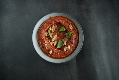 A bowl of rich, dark satay marinade with fresh herbs and spices around it.