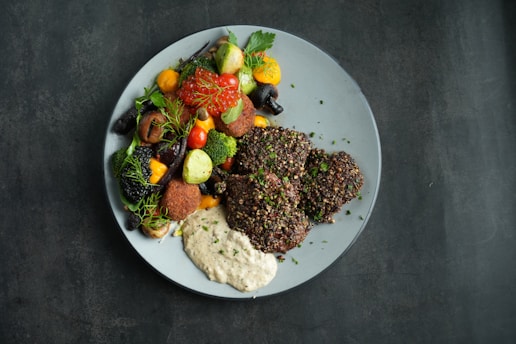 A beautifully plated main course with grilled meat, roasted vegetables, and a drizzle of sauce.